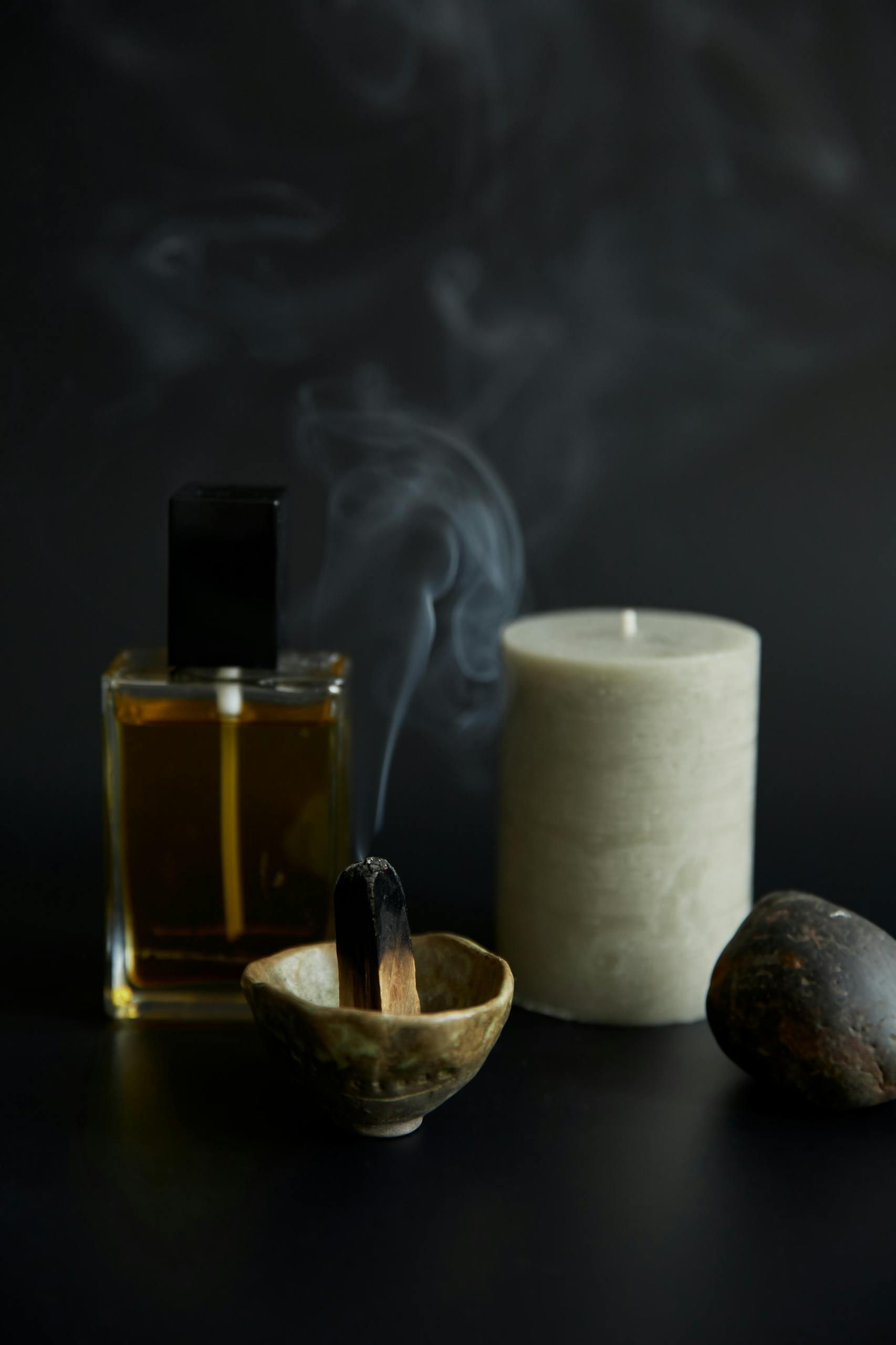A calming aromatherapy setup featuring a lit candle, incense, and essential oil on a dark background.