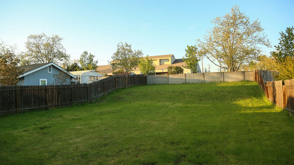 a grassy yard with a fence and a house in the background
