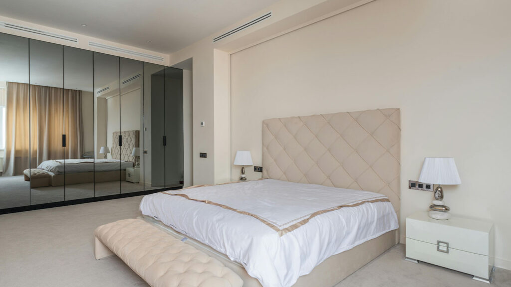 Cozy bed and ottoman bench in elegant bedroom with wardrobe