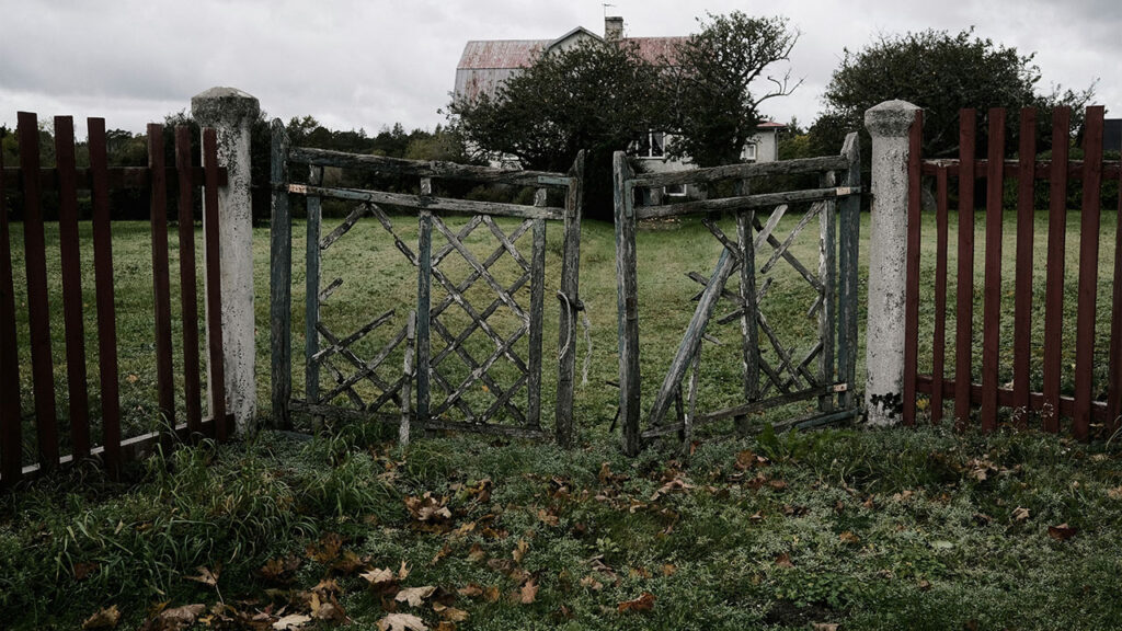 a wooden gate in a grassy field with a house in the background