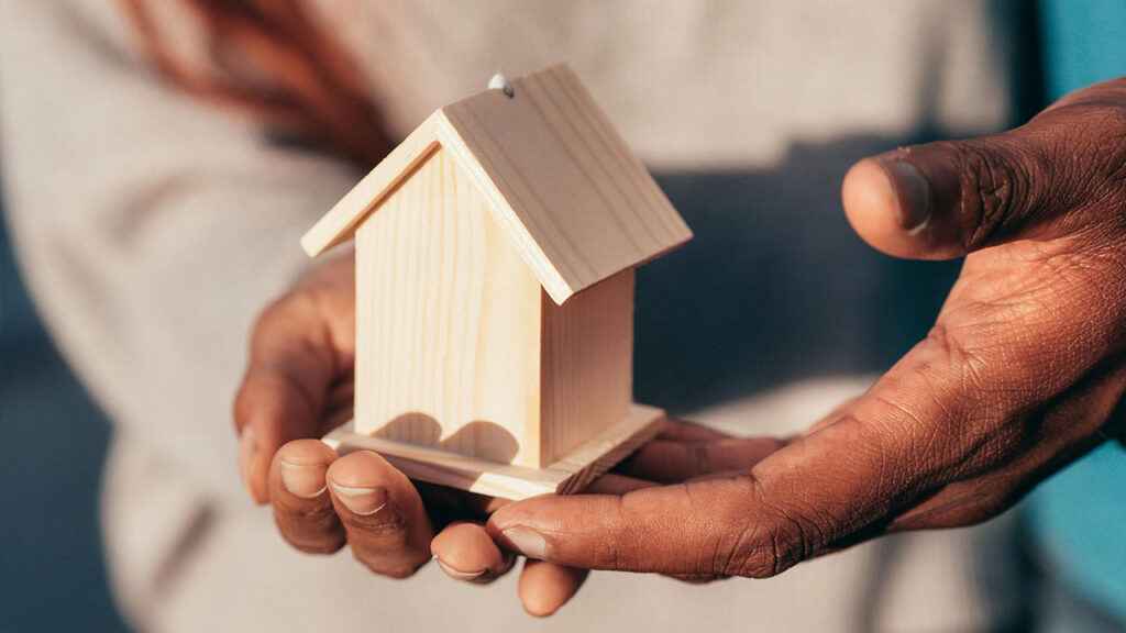 People Holding a Miniature Wooden House