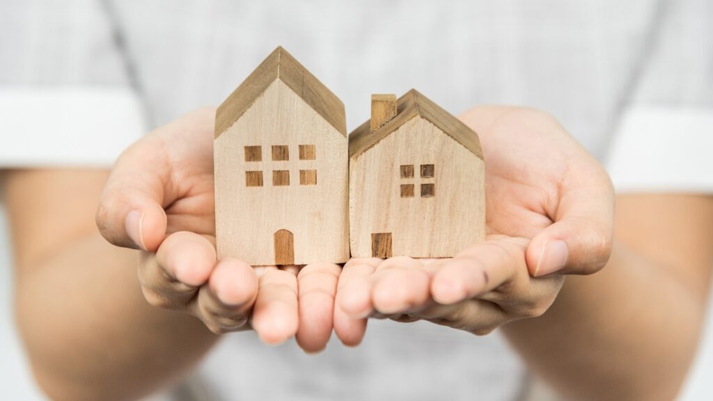 Close up hand presenting wooden house model in her hand, real estate concept.