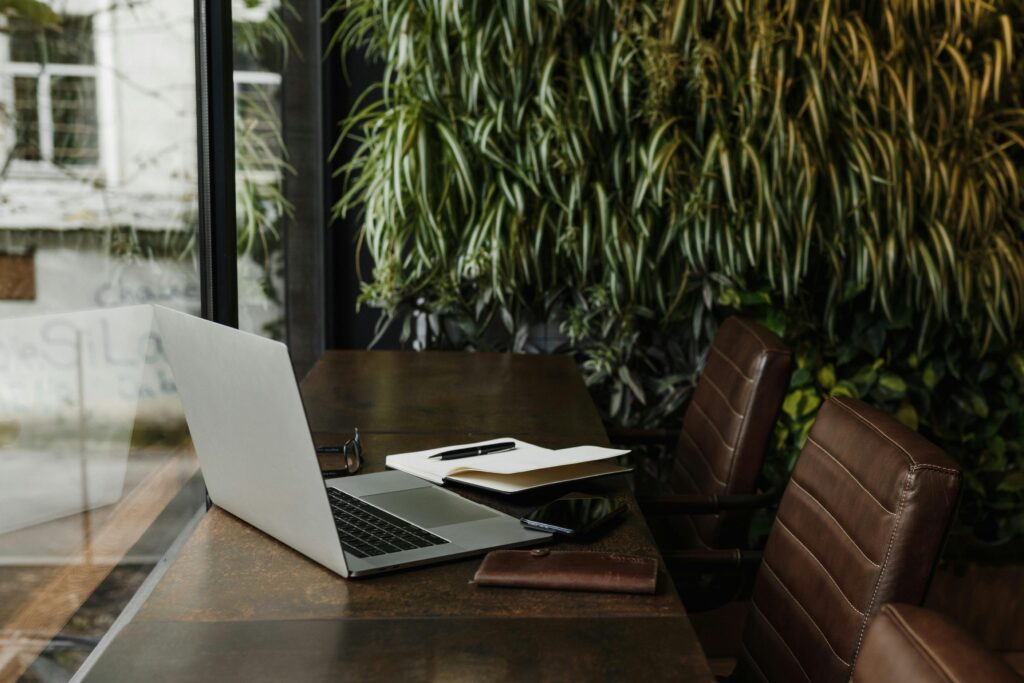 Arina Krasnikova / Pexels A laptop and other office supplies on top of a table with a plant wall in the background.