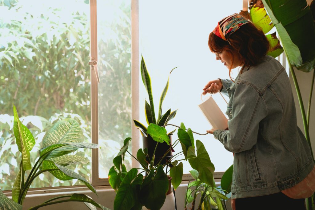 A woman watering plants by the window.