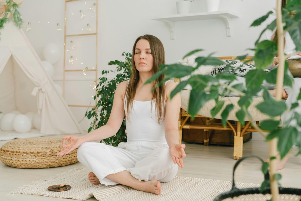 A woman meditating surrounded by plants.