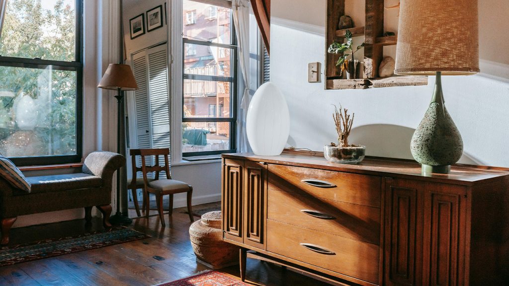 Elegant table lamps placed on wooden cabinet in stylish room with windows in sunlight