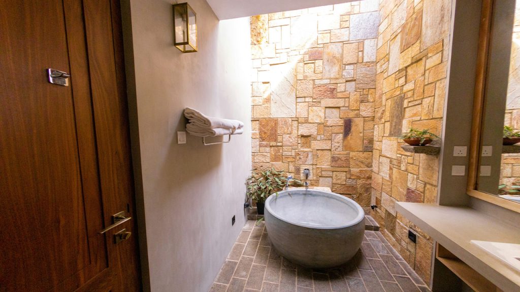 white ceramic bathtub beside brown brick wall