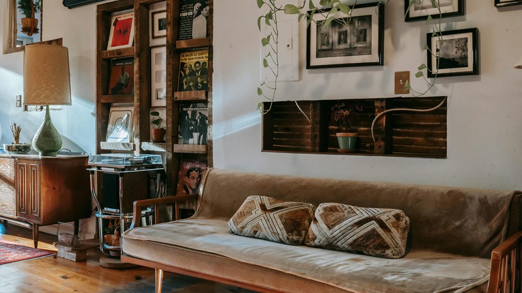 Shelf with vinyl records collection between comfortable sofa and wooden cabinet in vintage styled room