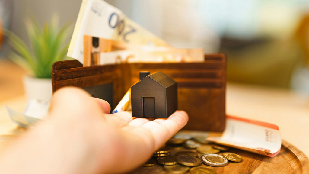 A person holding a small house and some money