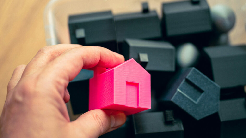 A person holding a pink house in front of a pile of black cubes