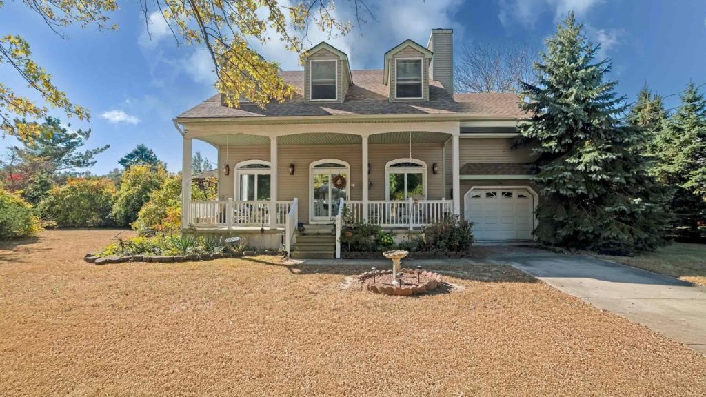 A charming country-style home with a front porch and dormer windows, surrounded by greenery.