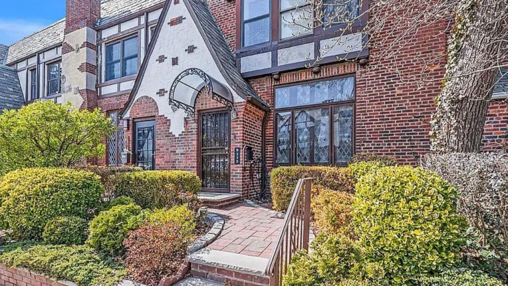 Tudor-style brick home with an arched entryway, leaded glass windows, and lush landscaping.