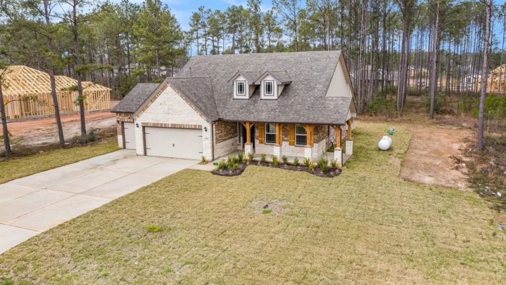 A cozy cottage with stone and brick exterior, a three-car garage, and a front porch surrounded by pine trees.