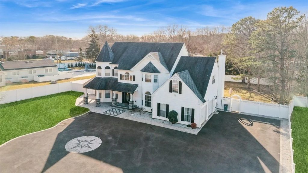 Aerial view of a Victorian-style colonial home in Holtsville, NY, featuring a turret, white facade, black shutters, and a decorative driveway.