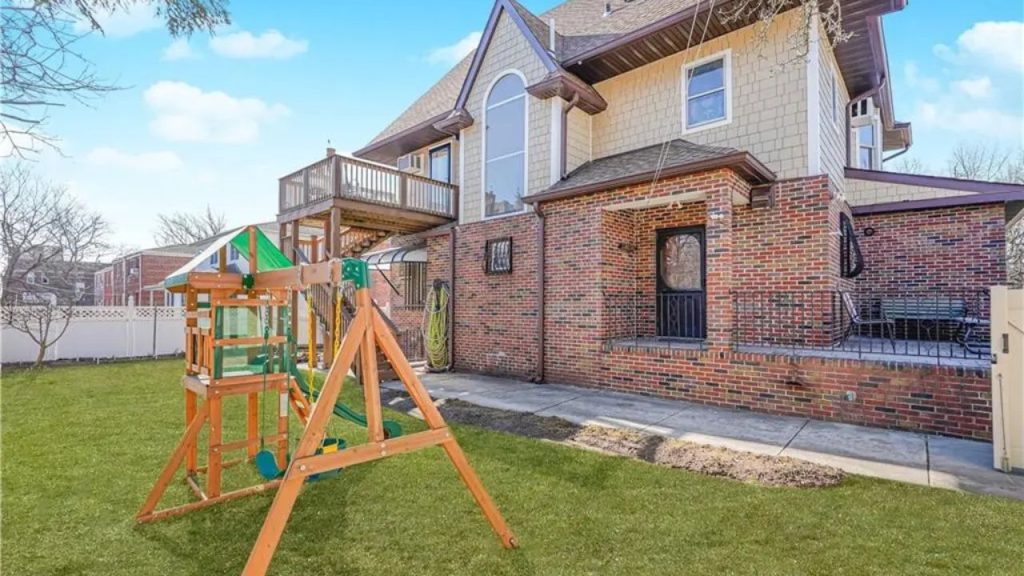 Backyard with a wooden playset, brick patio, and a well-maintained lawn.