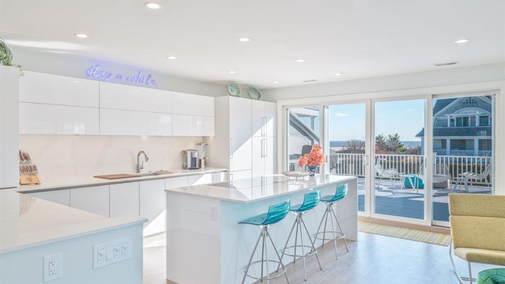 A bright modern kitchen with a large island, turquoise barstools, and ocean views.