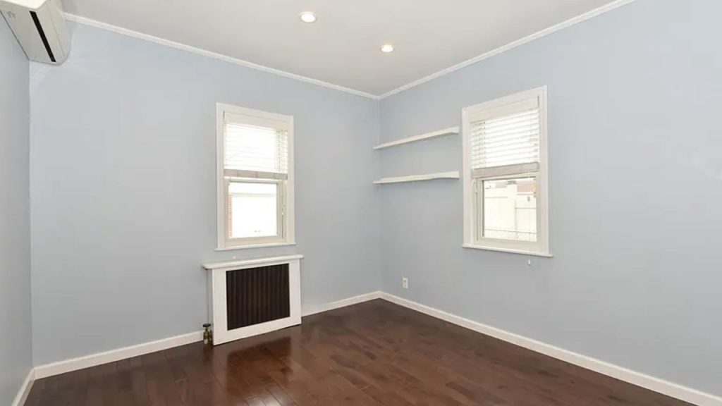 Bright bedroom with soft blue walls, hardwood floors, and built-in shelves.