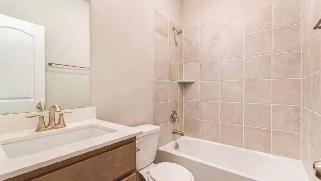 Bathroom with a tiled shower and tub, wood-finished vanity, and brass faucet.