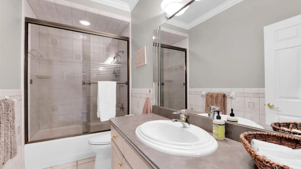 Well-lit bathroom with a glass-enclosed shower, vanity, and storage baskets.
