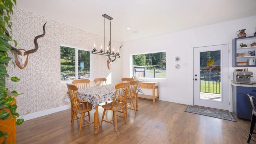 Bright dining area with wooden furniture, a patterned accent wall, and large windows showcasing outdoor views.