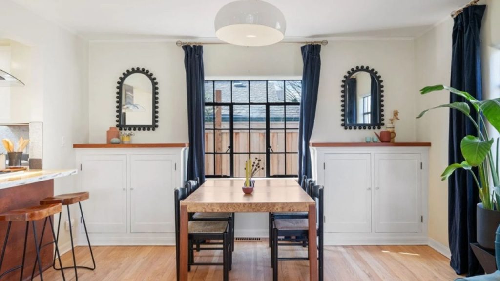 Bright dining area with a wooden table, built-in cabinets, and black-framed mirrors.