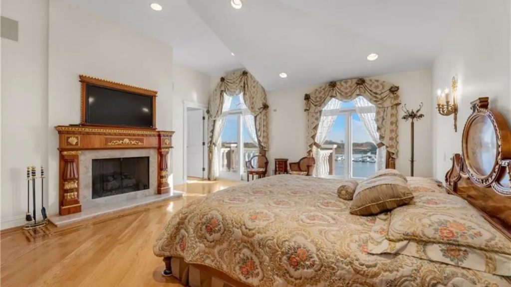 Elegant bedroom with a fireplace, ornate bed, and water views.