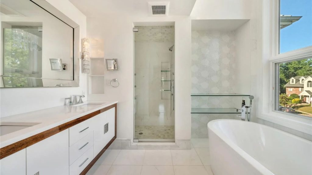 A bright, modern bathroom with a freestanding tub, glass-enclosed shower, and dual vanity with wood accents.