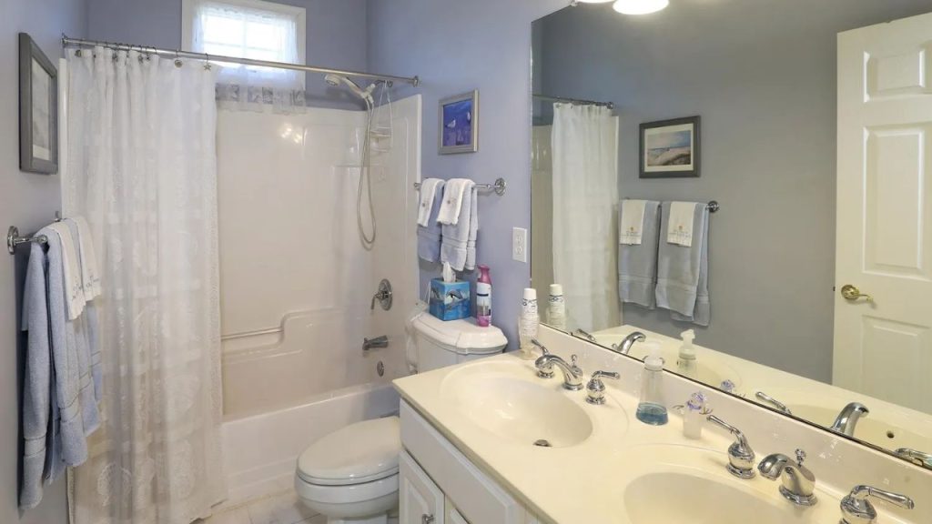 Light blue bathroom with double vanity, lace shower curtain, and soft lighting.