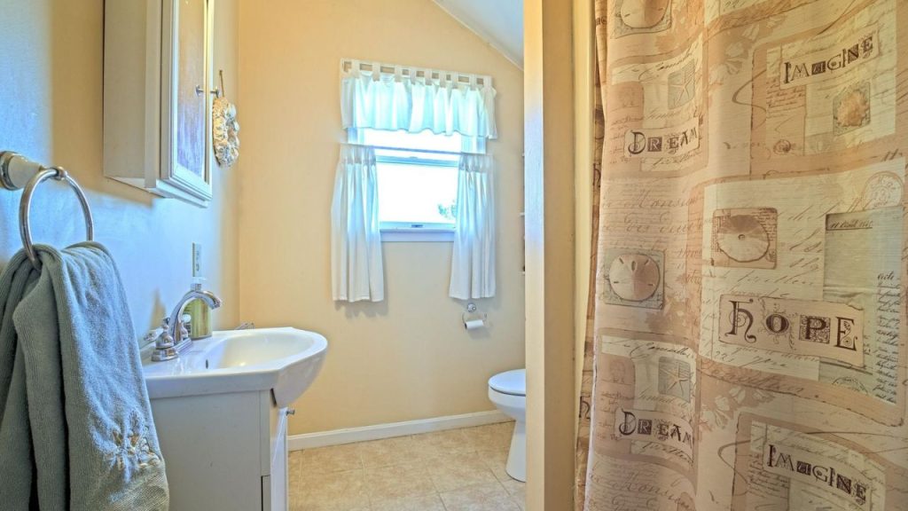 Small bathroom with soft lighting, white curtains, and a cozy shower curtain.