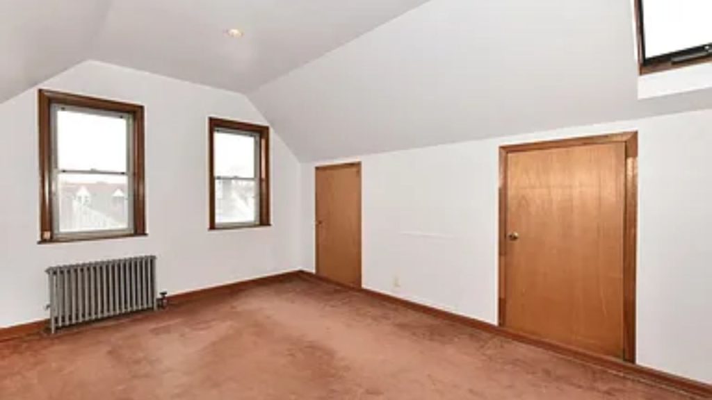 Attic room with sloped ceiling, brown carpet, wooden doors, and a skylight.
