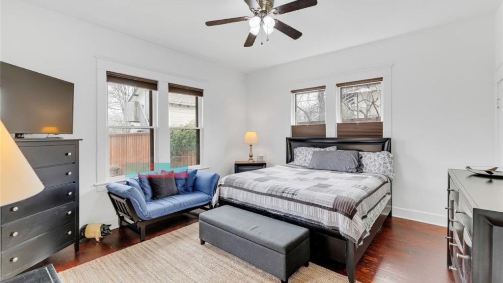 Bright bedroom with king bed, blue futon, hardwood floors, and large windows.