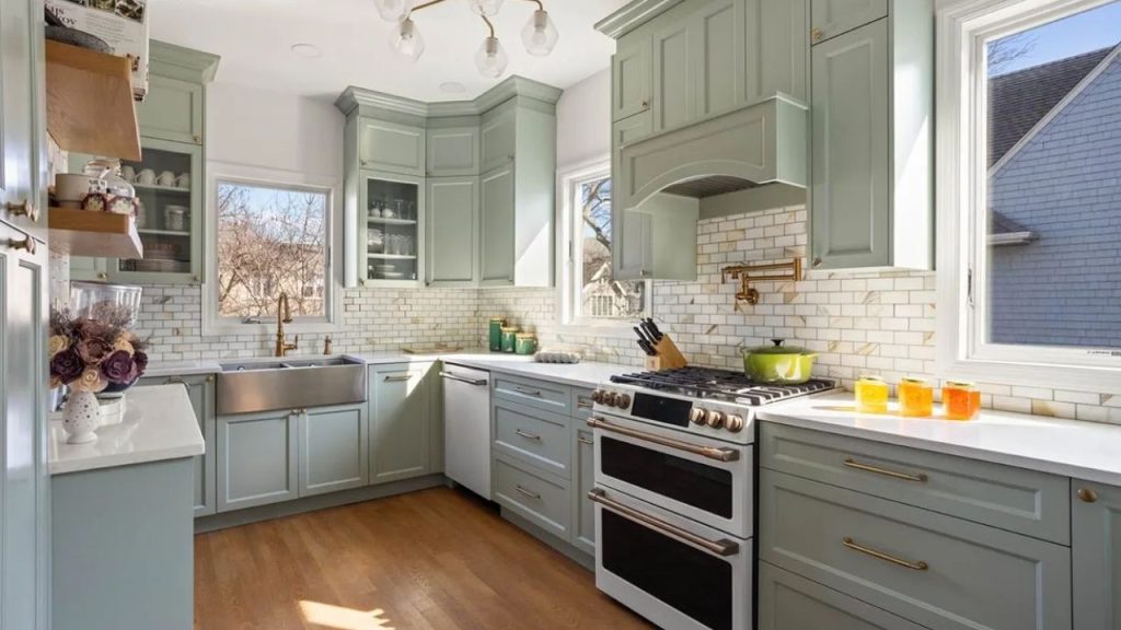 Bright kitchen with sage-green cabinets, brass fixtures, and a farmhouse sink.