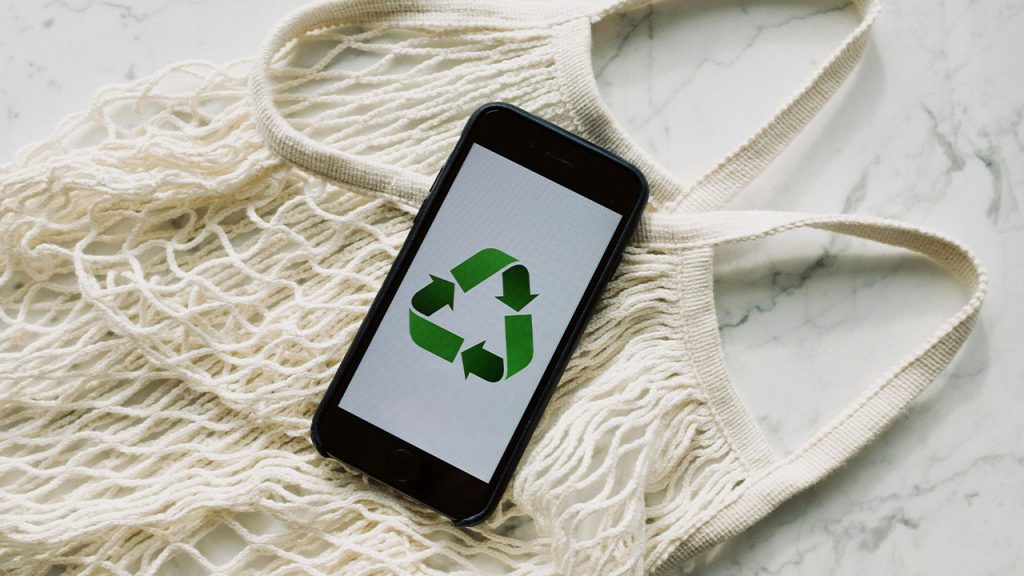 martphone with recycling sign on screen placed on white mesh bag on marble table