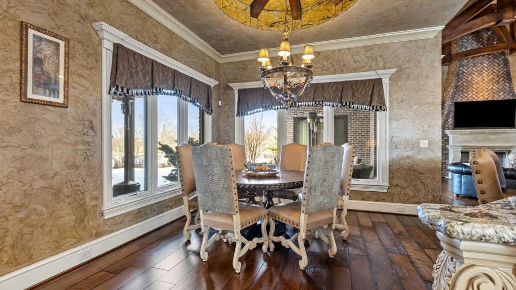 Dining area with round table, upholstered chairs, and large windows.