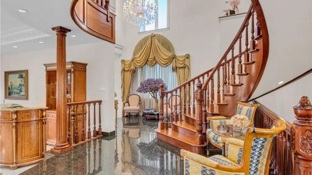 A grand foyer with a curved wooden staircase, chandelier, and classic furnishings.