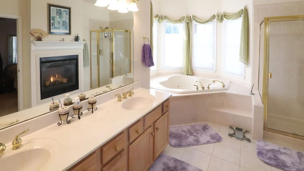 Luxurious bathroom with a corner soaking tub, gold-accented shower, and a cozy fireplace.