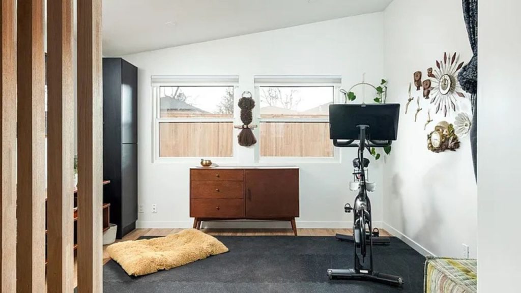 Bright home gym with a stationary bike, mid-century dresser, and vintage wall accents.

Would you like me to describe the next image as well?