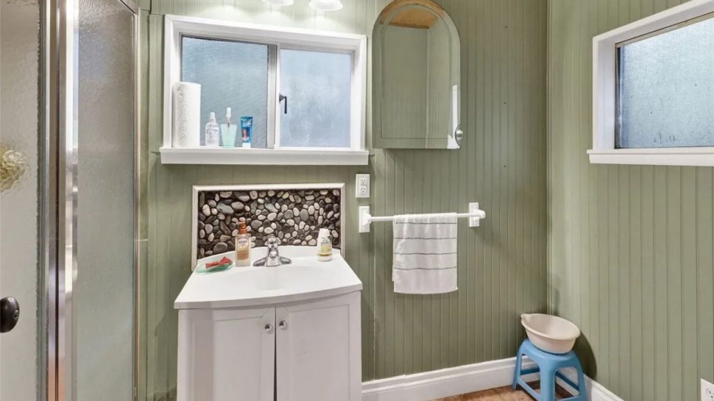Cozy bathroom with green walls, pebble backsplash, and frosted windows.