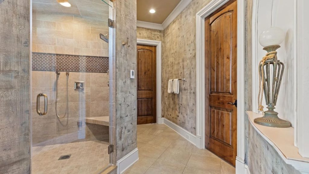Bathroom with glass shower, wooden doors, and mosaic tile accent.