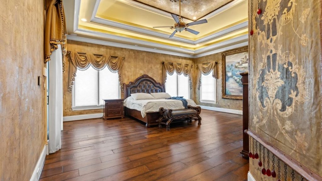 Luxurious classical bedroom with a grand wooden bed, ornate drapery, textured walls, and a decorative ceiling.