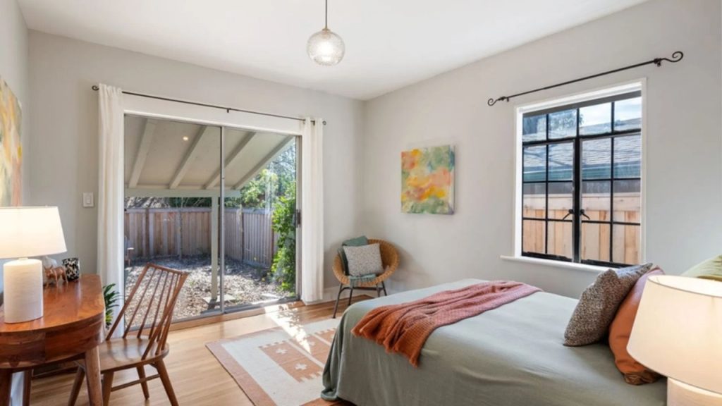 Bright and cozy bedroom with soft pastel accents, featuring a sliding glass door that opens to the backyard.