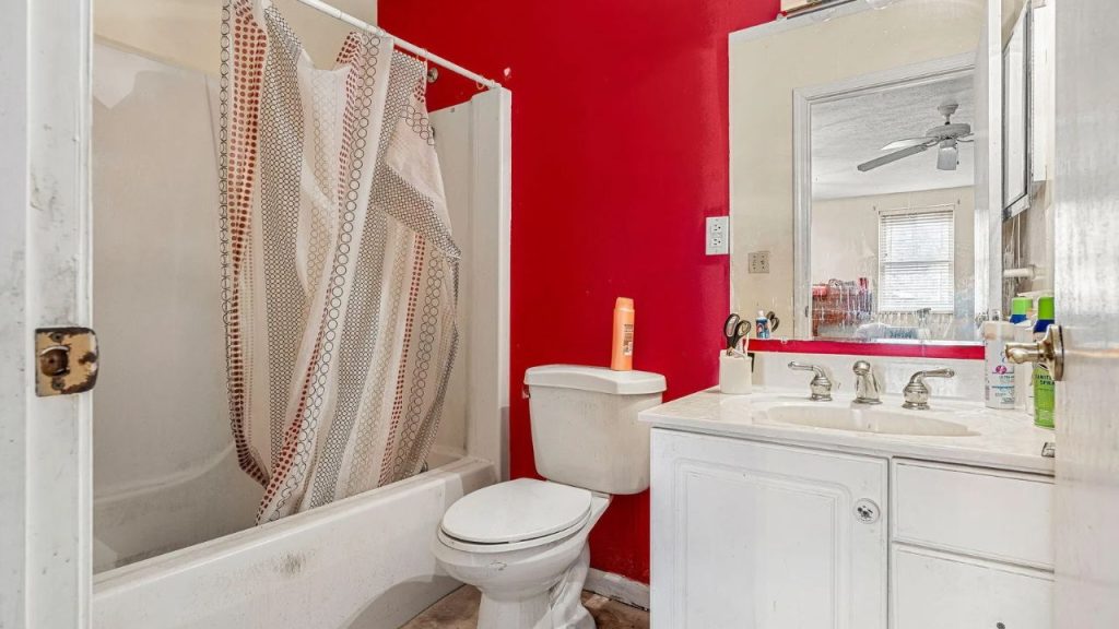 Small bathroom with a red accent wall, white vanity, and bathtub.