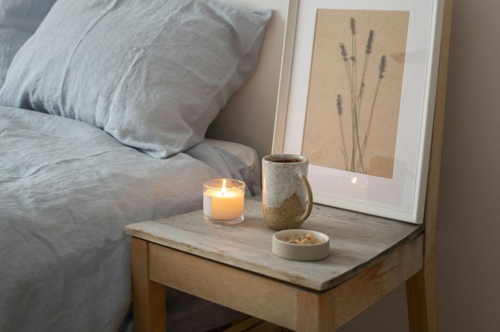 A table beside a bed with a mug and other decorations.