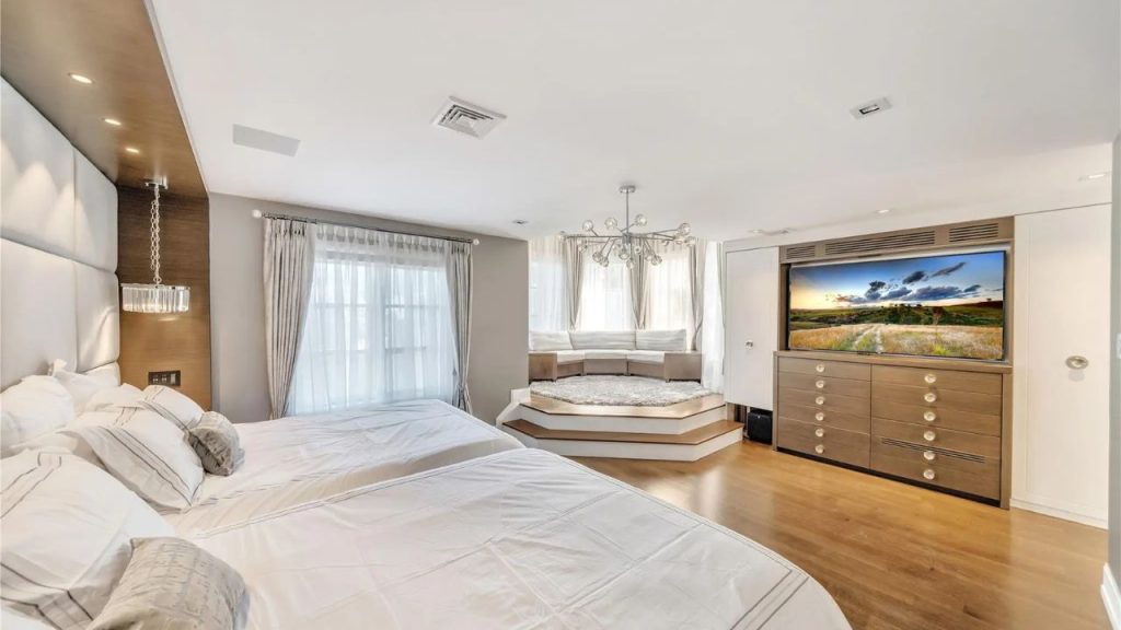 A modern bedroom with a raised seating nook, double bed, built-in TV, and elegant lighting.