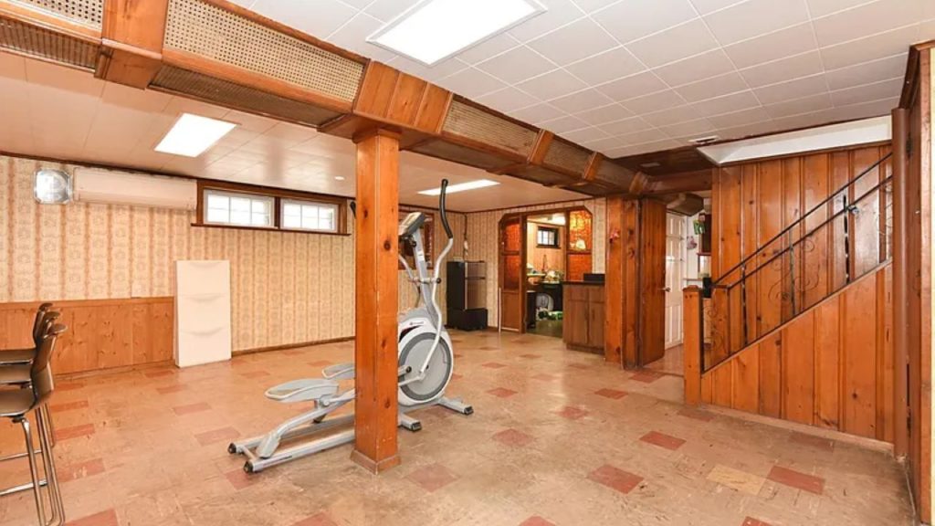 Wood-paneled basement with vintage decor, an exercise machine, and a small bar area.