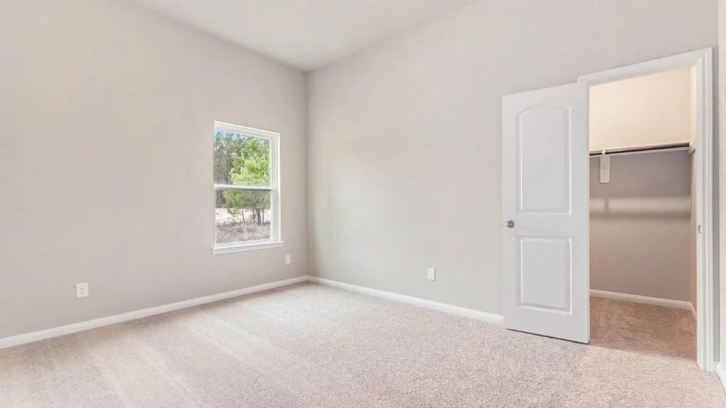 Neutral-toned bedroom with a window, walk-in closet, and carpet flooring.
