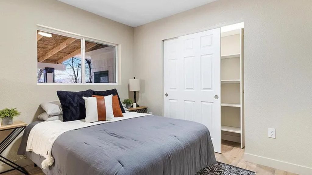 Modern bedroom with a gray bedspread, sliding closet, and large window.
