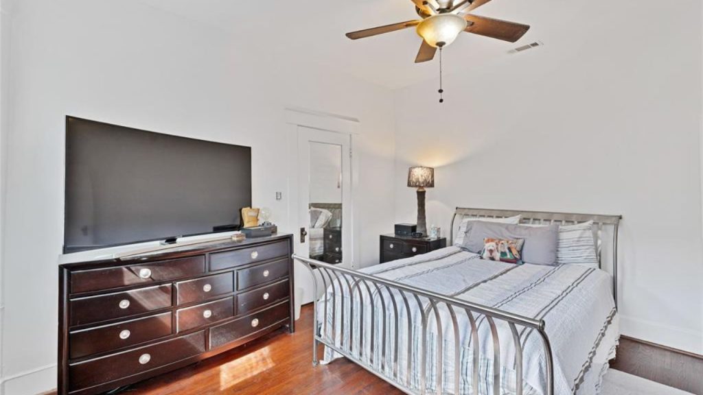 Bright bedroom with a metal bed frame, dark wood dresser, and large TV.