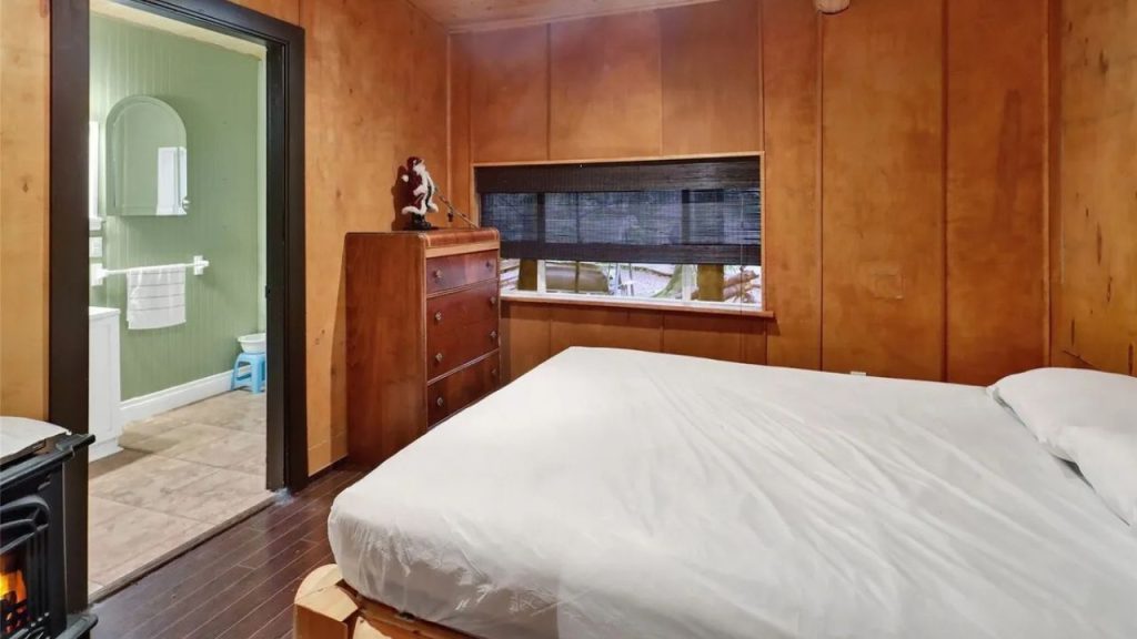 Rustic bedroom with wood-paneled walls, a large window, and a wood stove.