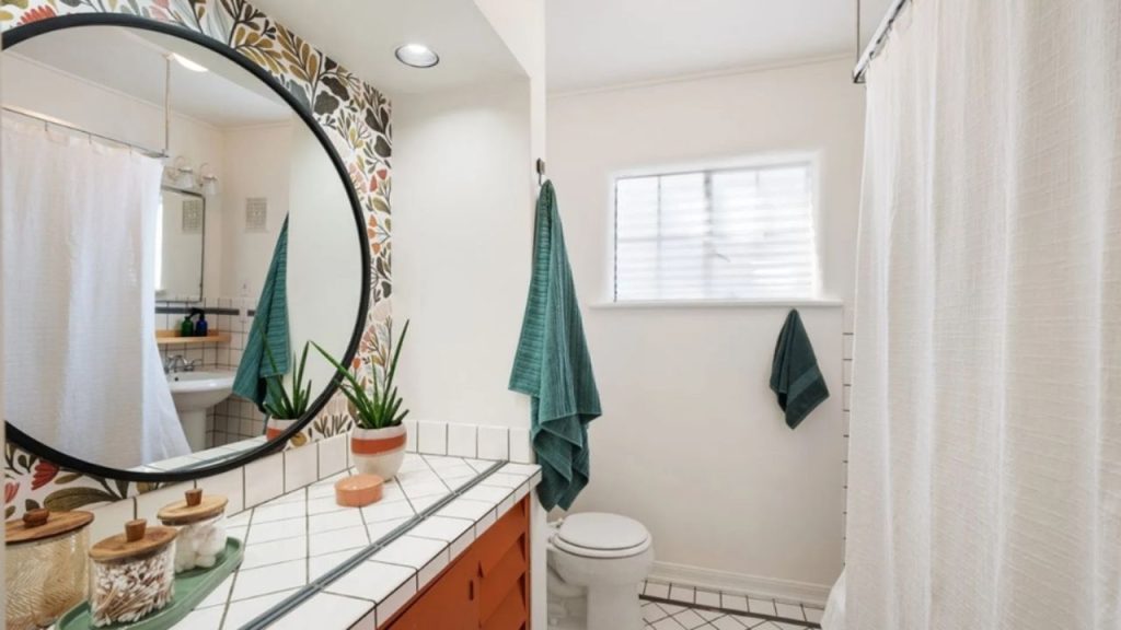 Bright bathroom with a bold floral accent wall, a round mirror, and stylish tile countertops. Teal towels add a pop of color.